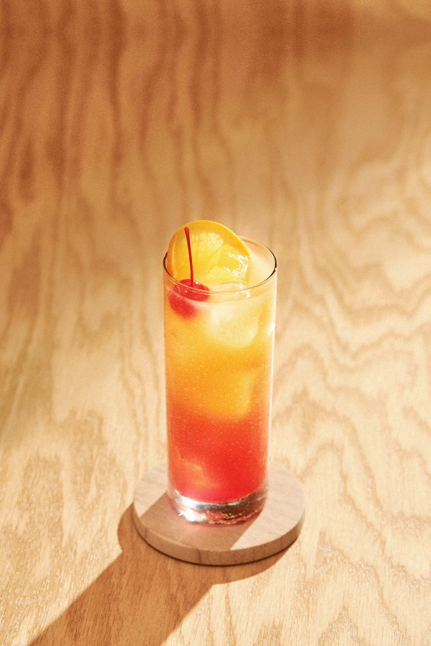Kentucky sunrise cocktail in a tall glass garnished with berries and an orange slice