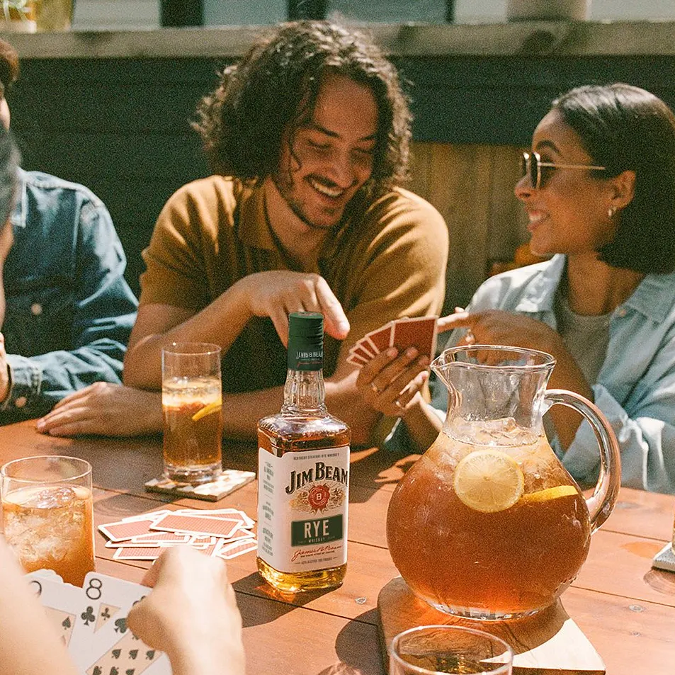 A relaxed gathering at a wooden table with drinks, a pitcher, and playing cards, evoking a casual social atmosphere.