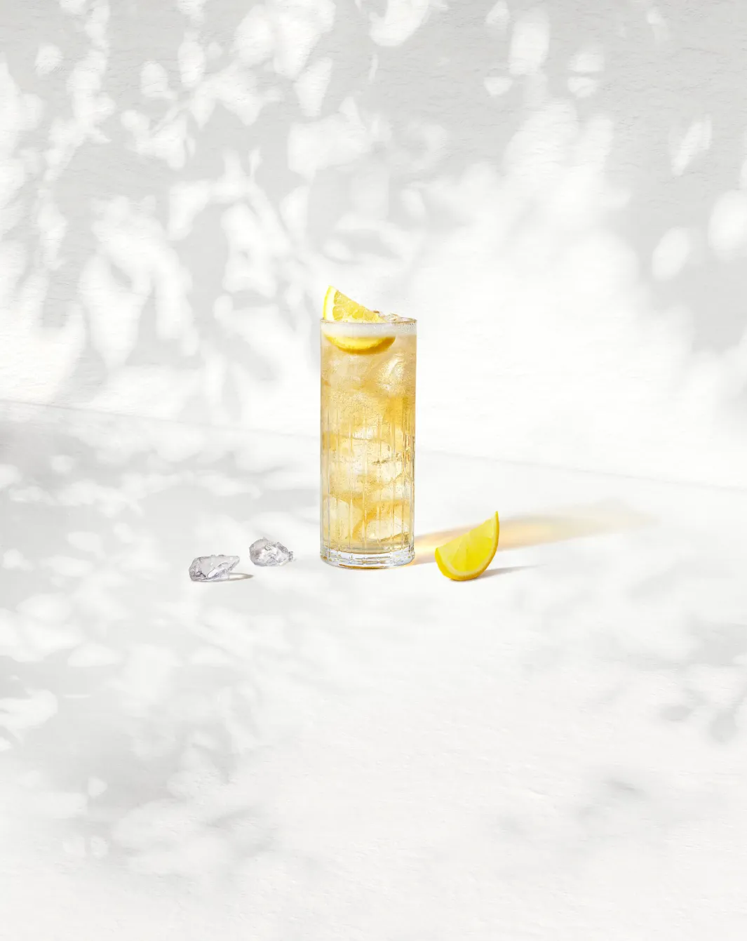 Jim Beam Bourbon & Soda Highball in a tall glass with ice and a lemon wedge, set against a sunlit backdrop.