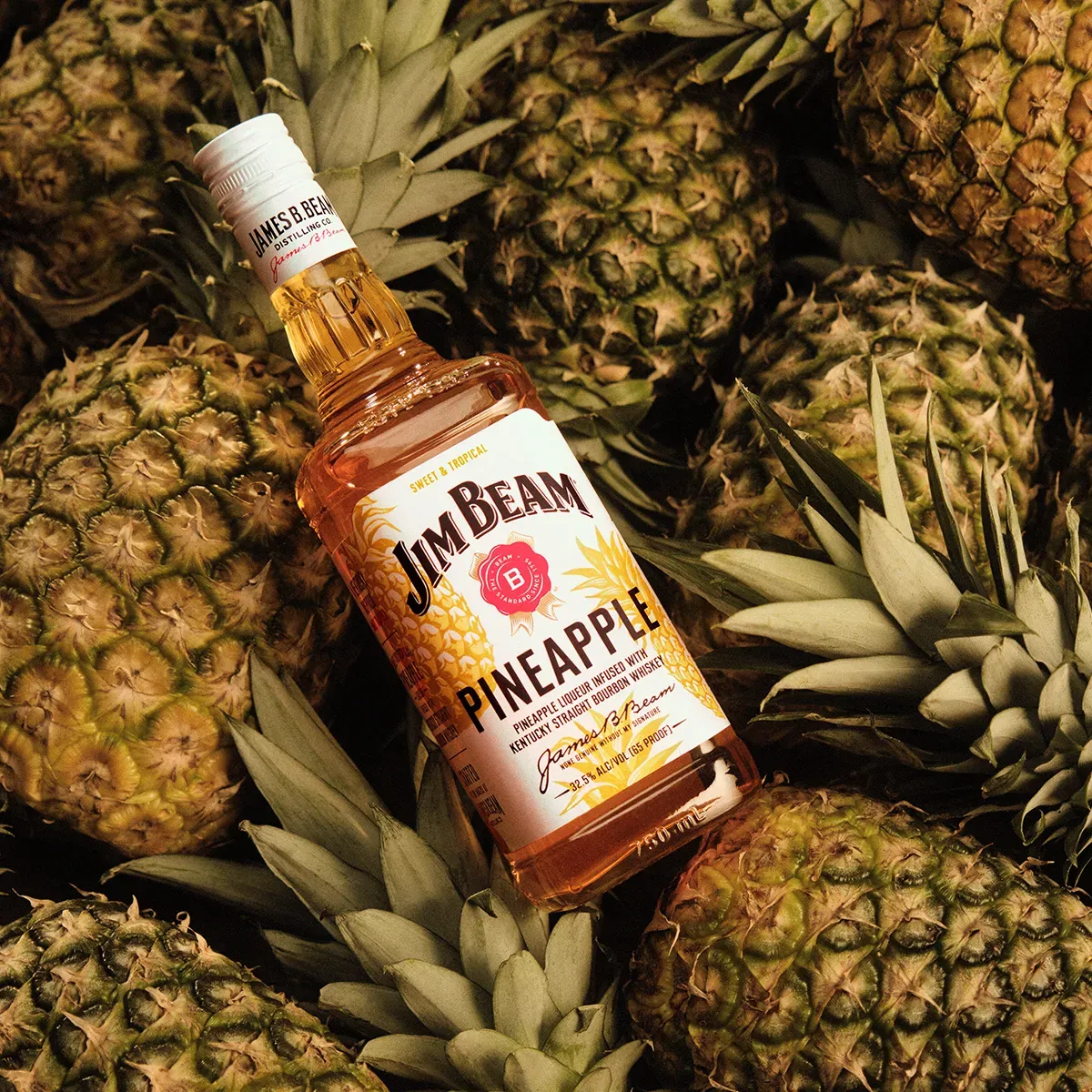 Jim Beam Pineapple bottle nestled among fresh pineapples—the sweet, tropical start to a Piña Colada cocktail recipe